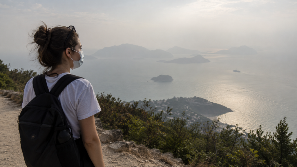 Haze Kembali Selimuti Labuan Bajo, BMKG Catat Jarak Pandang 4 Km 12 Seorang wisatawan mengenakan masker penutup wajah berdiri di titik pandang (viewpoint), memandangi laut dan perbukitan yang tertutup udara kabur.